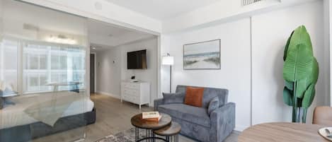 A modern living room with a grey sofa, a round coffee table, a TV mounted on the wall, and a large green plant.