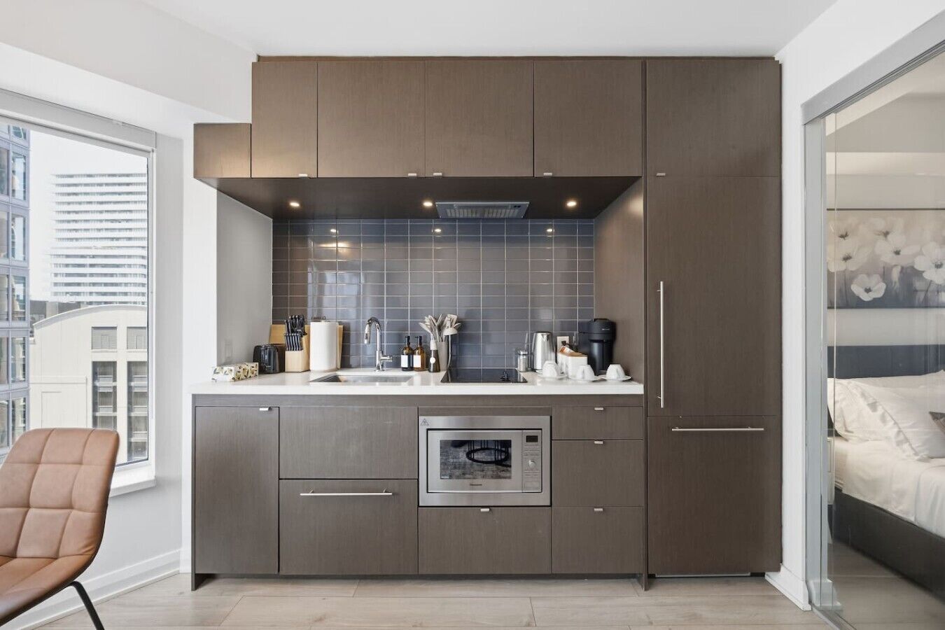 Eine moderne Küche mit grauen Schränken, einem eingebauten Backofen und einem Fenster mit Blick auf die Stadt.