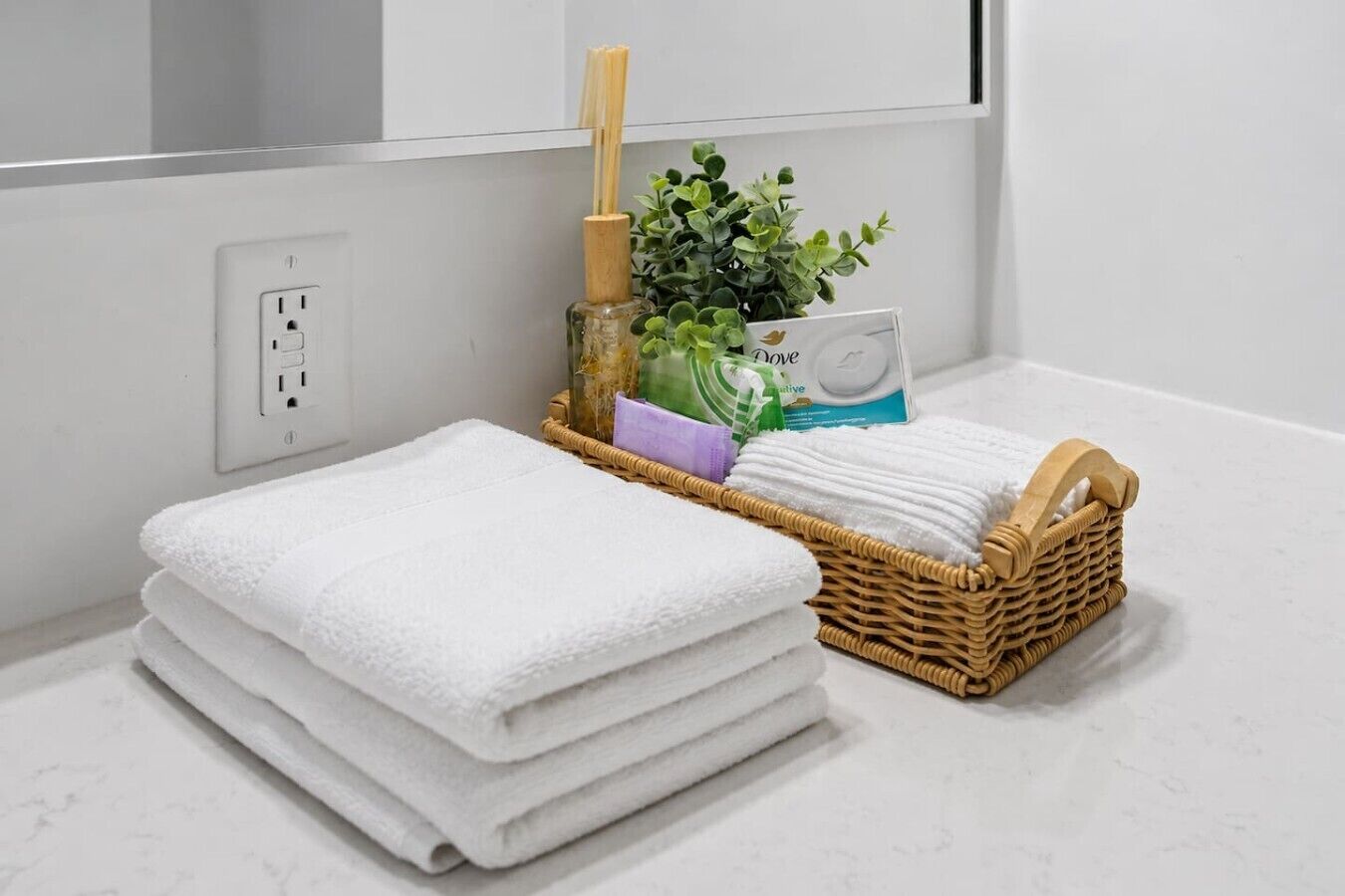A bathroom with a stack of white towels, a wicker basket with toiletries, and a plant.
