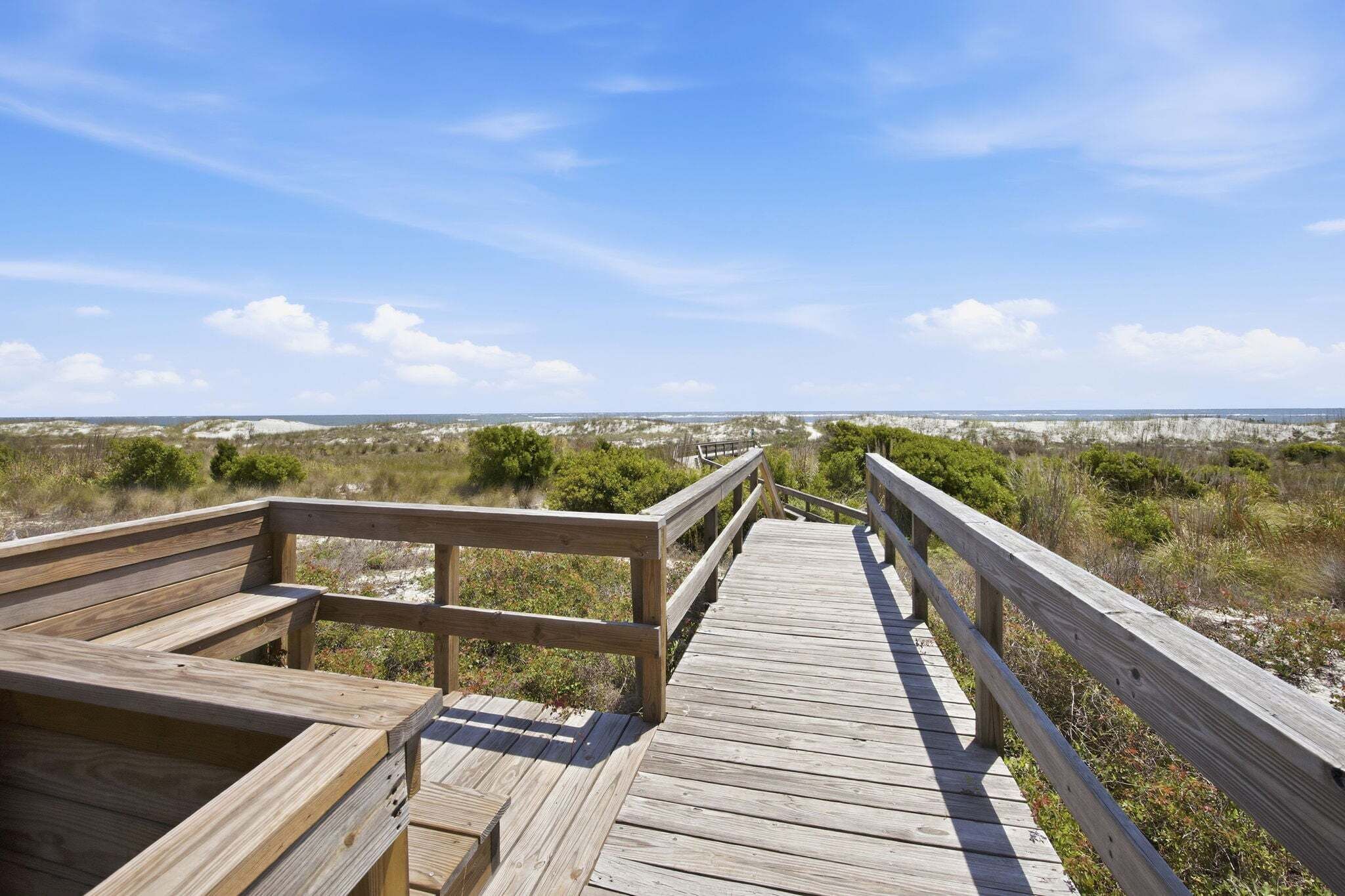 A wooden boardwalk leading to a beach with a clear view of the ocean and distant land.