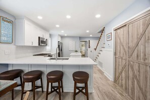 A kitchen with a large island, bar stools, white cabinets, and a wooden barn-style door. - Modern Oceanfront Beach Club Villa *Unit 64* in Wild Dunes w/Community Pool! Ocean Views & Breezes! (Isle Of Palms)