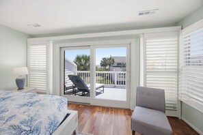 A bedroom with a bed, a chair, a nightstand, a lamp, and a balcony with a view of the outside. - Modern Oceanfront Beach Club Villa *Unit 64* in Wild Dunes w/Community Pool! Ocean Views & Breezes! (Isle Of Palms)
