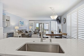 A modern kitchen with a large island, a dining area with a table and chairs, a sofa, and a fireplace. - Modern Oceanfront Beach Club Villa *Unit 64* in Wild Dunes w/Community Pool! Ocean Views & Breezes! (Isle Of Palms)