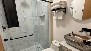 A bathroom with a glass shower enclosure, a toilet, a sink with a decorative basin, and a towel rack with folded towels. - Acogedor MiniLoft 202 (Ciudad de México)