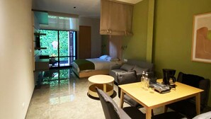A modern living space with a dining area, a sofa, and a view of greenery through large windows. - Acogedor MiniLoft 202 (Ciudad de México)