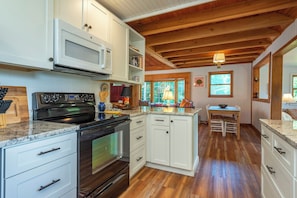 A kitchen with white cabinets, a black stove, and a wooden ceiling.