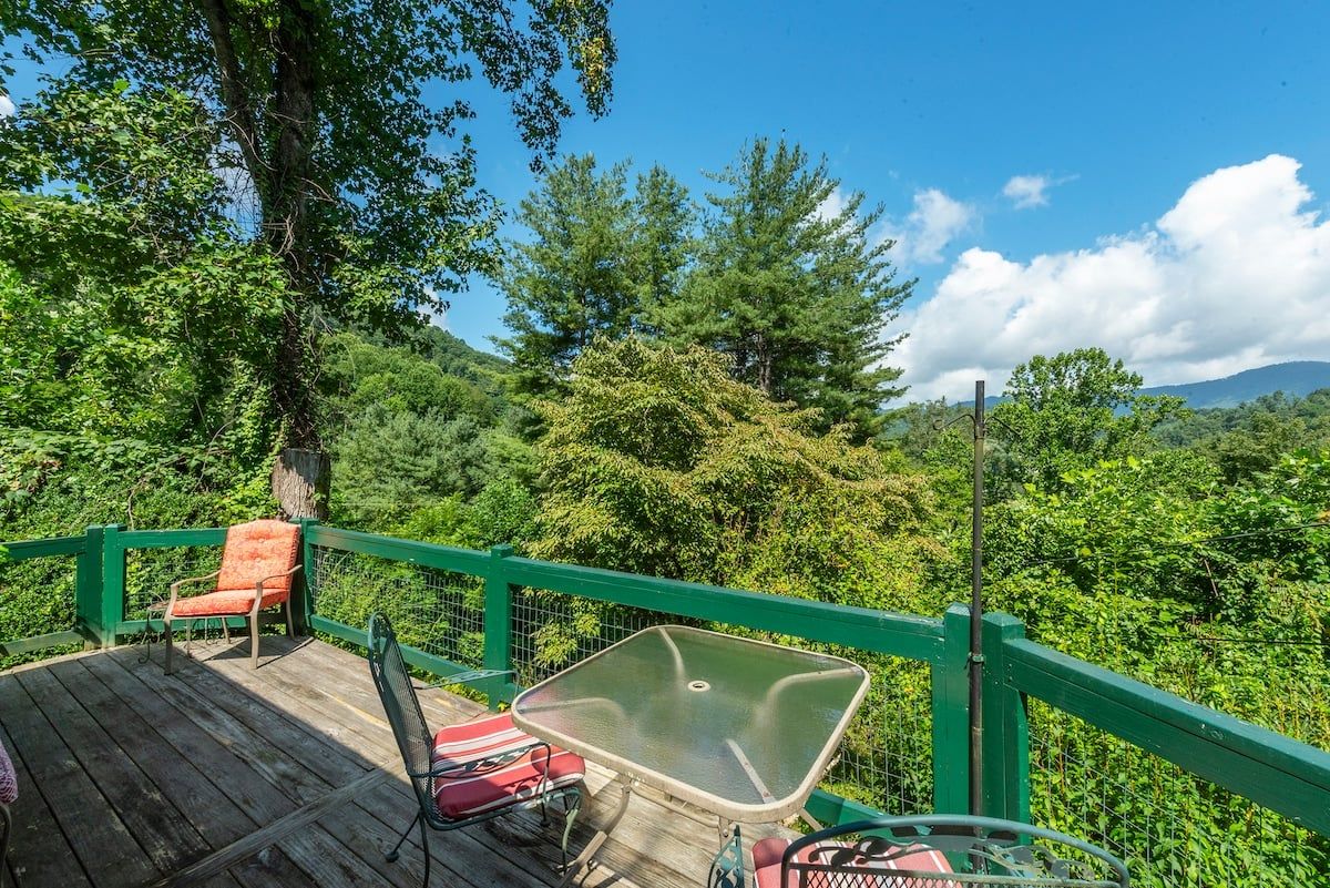 A wooden deck with a green railing, a glass table, and two chairs.