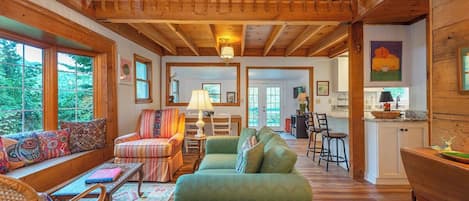 A spacious living room with a high ceiling, wooden beams, a green sofa, and a dining area with a wooden table and chairs.