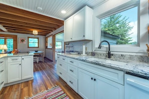 A kitchen with white cabinets, a granite countertop, a window with a view of trees, and a wooden ceiling.
