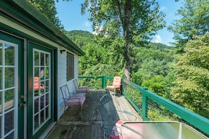 A wooden deck with outdoor seating, a green railing, and a view of a forested hillside.
