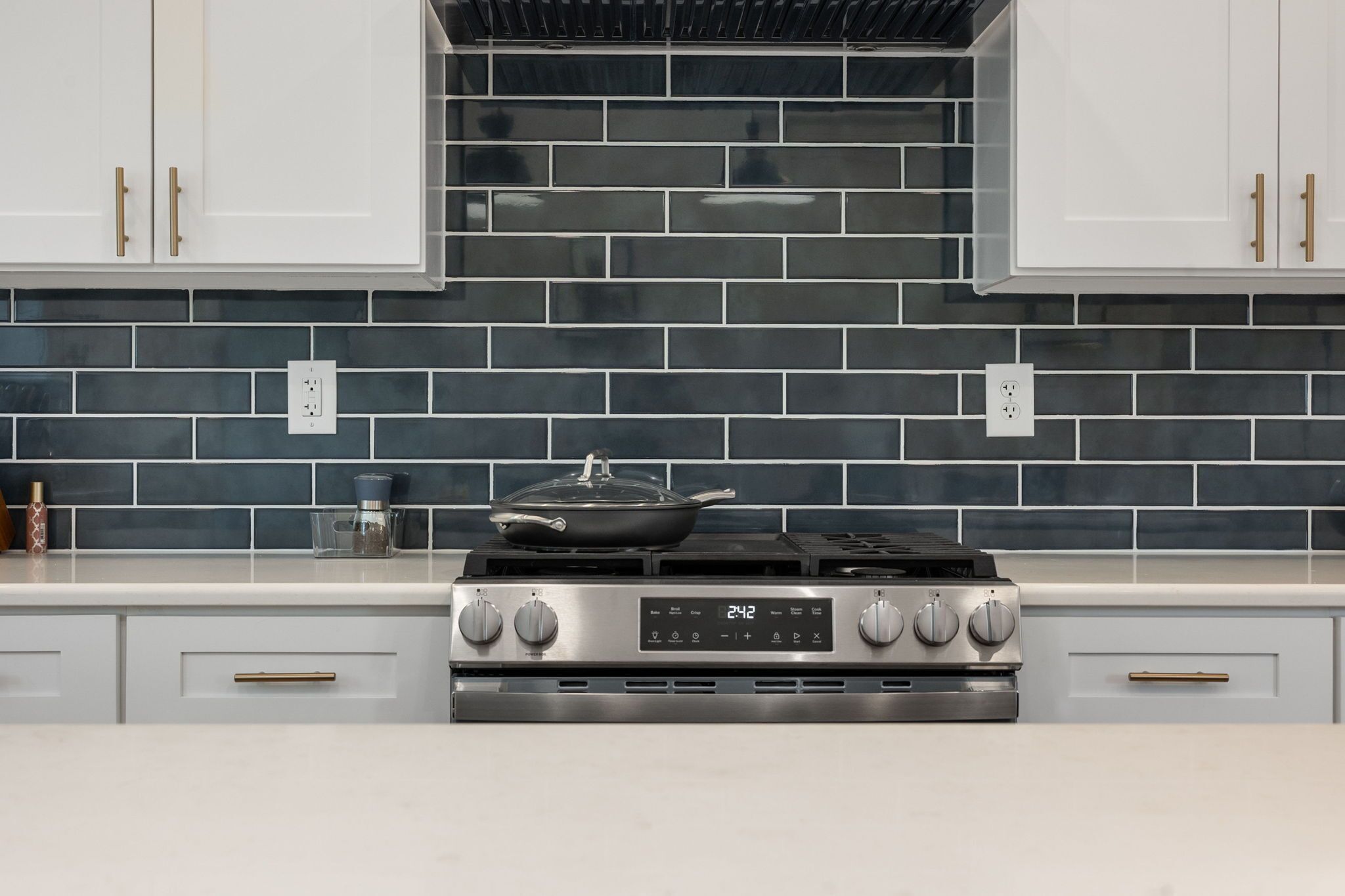 A kitchen with a stove, white cabinets, and a tiled backsplash.