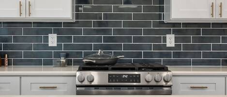 A kitchen with a stove, white cabinets, and a tiled backsplash.