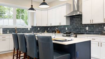 A modern kitchen with white cabinets, a black tiled backsplash, and a central island with bar stools.