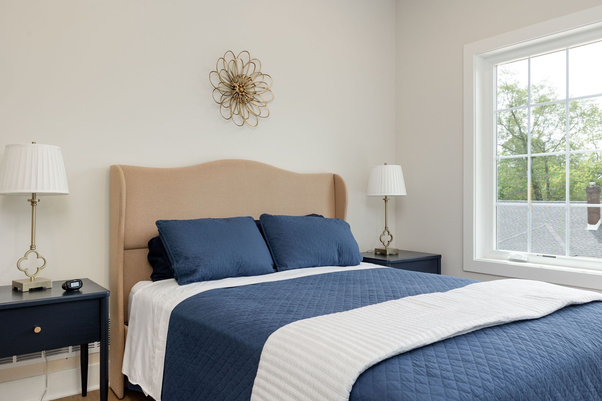 Une chambre à coucher comprenant un lit, deux tables de chevet, une fenêtre et un élément décoratif mural.