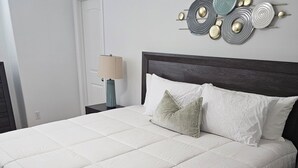 Ein ordentlich bezogenes Bett mit weißer Decke, einem dunklen Holz-Kopfteil und einem an der Wand befestigten abstrakten Kunstwerk.