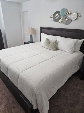 A neatly made bed with a white duvet, a dark wooden headboard, and a wall-mounted abstract art piece. - Charming 4-bedroom house with AC in lively Houston.  World Cup Central. (Houston)
