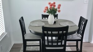 Ein Essbereich mit einem runden Tisch, vier Stühlen, einer Blumenvase und einem großen, abstrakten Gemälde an der Wand.