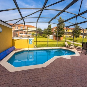 Ein Schwimmbecken mit Glasabdeckung, umgeben von einer Ziegelterrasse und einer gelben Wand.