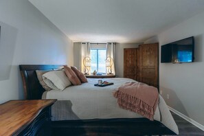 A bedroom with a bed, a bedside table, a TV mounted on the wall, and a window with curtains. - Dakmel Terrace Retreat (Southgate)