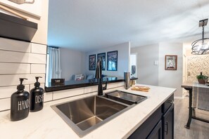 A modern kitchen with a stainless steel sink, black soap dispensers, and a marble countertop. - Dakmel Terrace Retreat (Southgate)