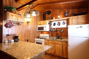 A kitchen with wooden cabinets, a granite countertop, a stove, a microwave, and a refrigerator. - Moose Haven Cabin, full kitchen, cover carport, Restmore Inn, Hill City (Hill City)