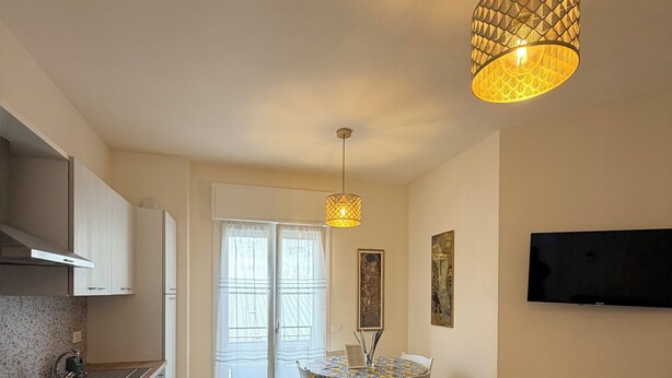 A modern kitchen with a dining area, a TV mounted on the wall, and a small bench with electronic devices. - Modern Sea Apartment (Punta Marina)