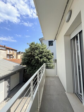 Ein Balkon mit Metallgeländer, einer weißen Markise und einem großen Baum im Hintergrund.