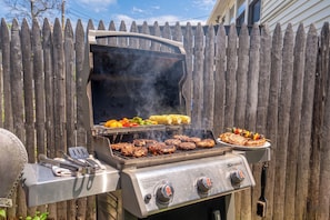 Ein Grill mit mehreren Kochzonen, integriertem Thermometer und einem Seitentisch mit Zange und Bürste.