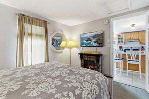 Ein Schlafzimmer mit Bett, Kamin, einem Gemälde, einem Spiegel und Blick zur Küche.