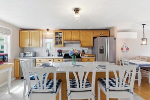 Eine moderne Küche mit Holzausstattung, einer zentralen Kochinsel mit Stühlen, einem Kühlschrank und einem Esstisch ebenfalls mit Stühlen.