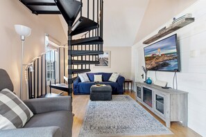 Ein Wohnzimmer mit Wendeltreppe, einer Couch, einem Couchtisch, einem Fernseher und einem Kamin.