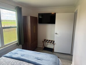 A bedroom with a bed, a wardrobe, a television mounted on the wall, and a window with a view of the outdoors.