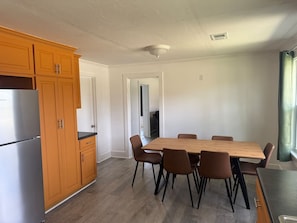 Une cuisine avec des meubles en bois, un réfrigérateur en acier inoxydable, une table à manger avec des chaises et une vue sur un couloir.