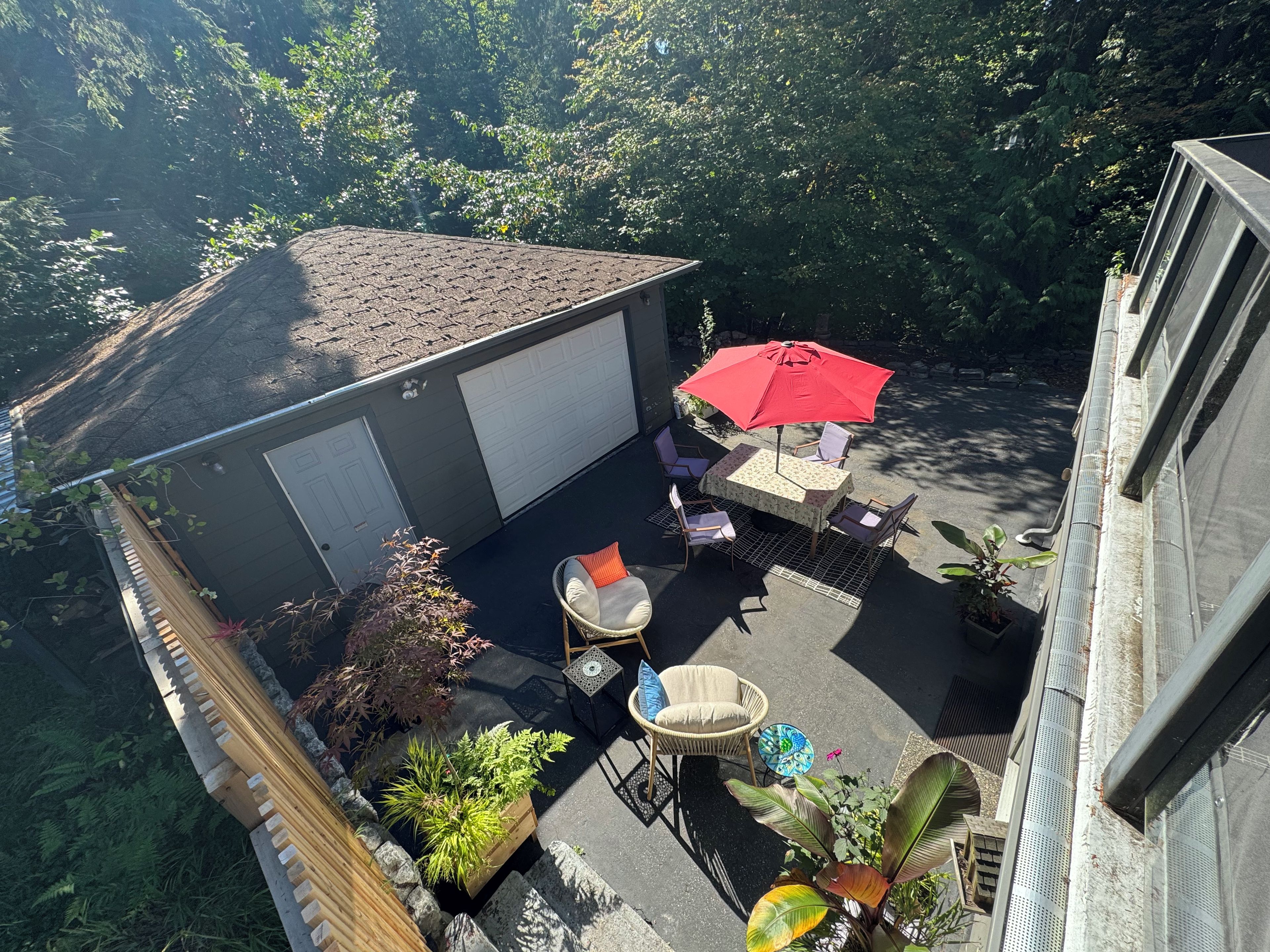 Eine Terrasse mit Tisch und Stühlen, umgeben von Kübelpflanzen und einem roten Sonnenschirm.