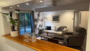 Ein modernes Wohnzimmer mit Sofa, Sessel, Couchtisch und einer Holztresore mit Gläsern und einer Pflanze.