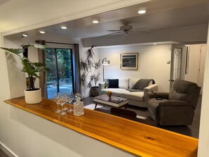 Una sala de estar moderna con sofá, sillón, mesa de centro y una barra de madera con vasos y una planta.