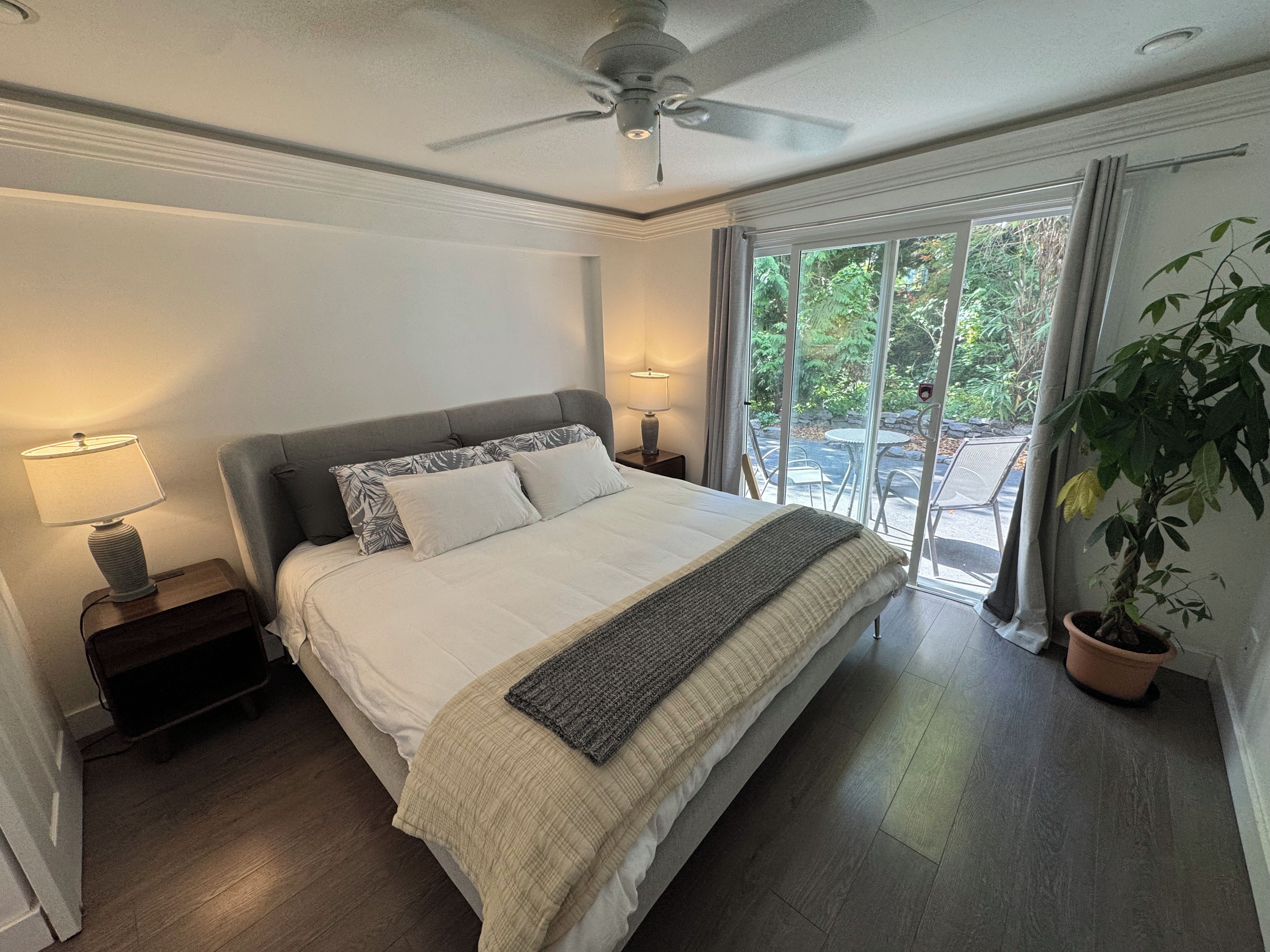 Ein Schlafzimmer mit einem Bett, zwei Nachttischlampen, einem Deckenventilator und Blick durch eine Glastür in einen Außenbereich.