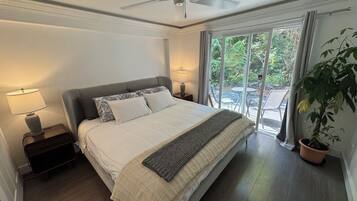 Ein Schlafzimmer mit einem Bett, zwei Nachttischlampen, einem Deckenventilator und Blick durch eine Glastür in einen Außenbereich.