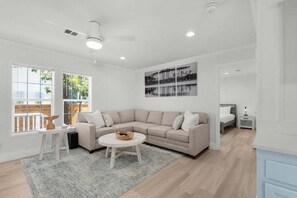 Ein modernes Wohnzimmer mit einem beigefarbenen Ecksofa, einem runden Couchtisch und einer weißen Wand mit einem gerahmten Bild.