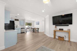 Eine moderne Küche mit hellblauen Schränken, einem Essbereich mit Tisch und Stühlen sowie einem an der Wand befestigten Fernseher.