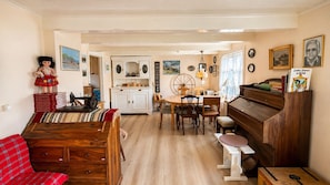 Una sala de estar acogedora con un sofá de madera, una mesa de comedor con sillas, un piano y una zona de cocina con armarios y una estufa.