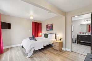 A hotel room with a bed, bedside table, lamp, artwork, and a view into the bathroom. - Dallas- Central Location, Spacious Backyard- Pets Welcomed (Dallas)