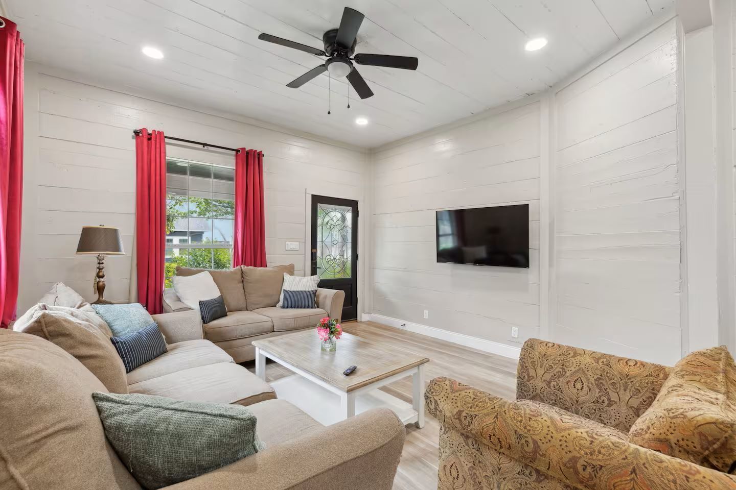 A living room with a sofa, armchairs, a coffee table, a TV, and a ceiling fan.