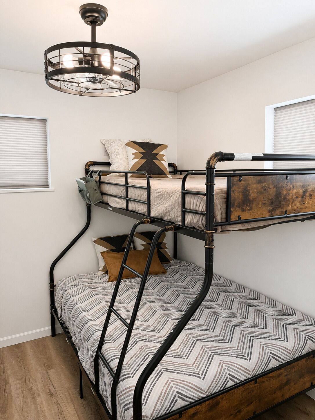 A bunk bed with a ladder, a hanging light fixture, and a window with blinds.
