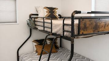 A bunk bed with a ladder, a hanging light fixture, and a window with blinds.