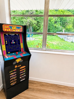 Une borne d’arcade avec le jeu Pac-Man, située dans une pièce dotée d’une grande fenêtre donnant sur un jardin.