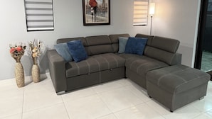 Un canapé modulable avec un coussin bleu et blanc, un tableau représentant un paysage urbain encadré, et deux lampes fixées au mur.