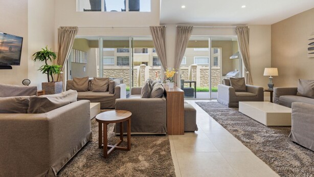 A spacious living room with a high ceiling, large windows, and a view of a balcony. - Upscale 3BR Suites, Patio With BBQ & Jacuzzi (Kissimmee)