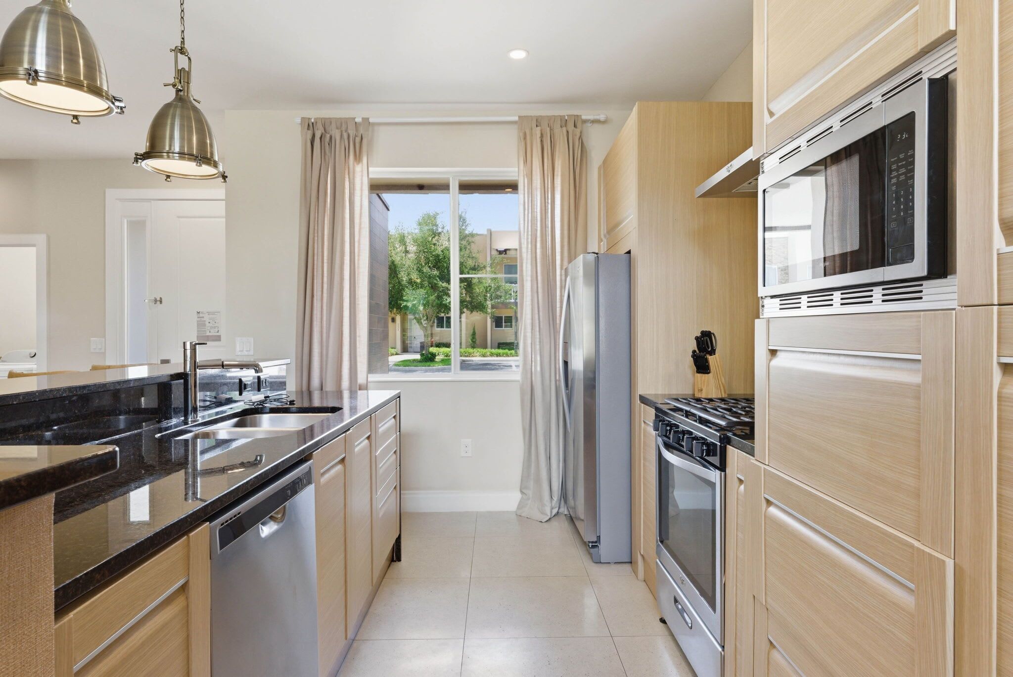 Een moderne keuken met een centraal eiland, roestvrijstalen apparatuur en uitzicht naar buiten.