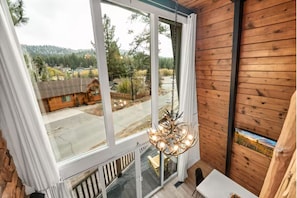 A room with a large window, a chandelier, and a painting on the wall. - Boutique Cabin, Across From Zoo, Mountain Views (Big Bear Lake)